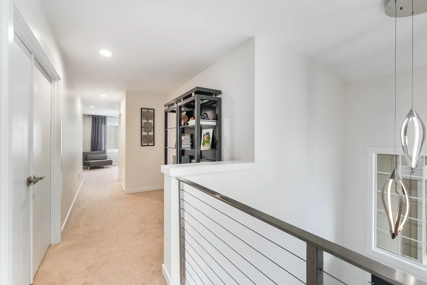 An upstairs landing painted white, with a cable-rail balustrade and a dark metal shelving unit