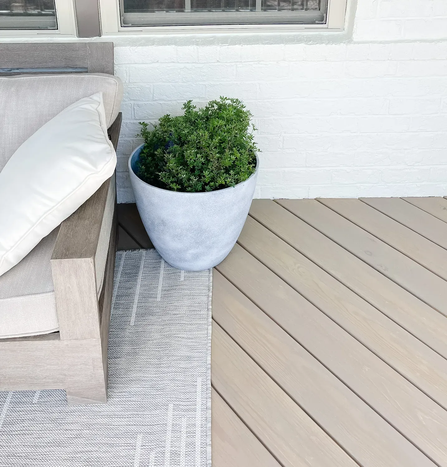A corner of the stained deck, the boards a pale weathered grey beside white brick