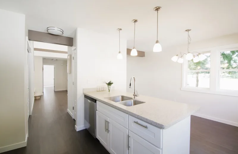 Peninsula sink and dishwasher under three pendants, hallway on the left, chandelier over the dining window