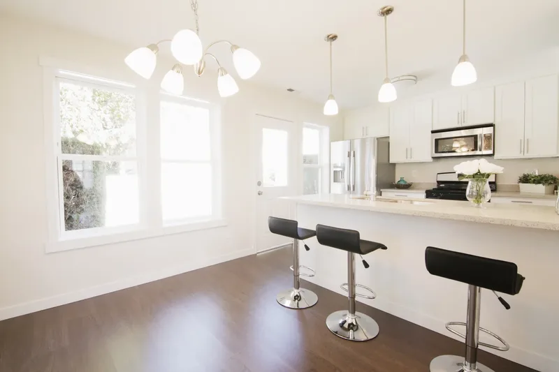 Dining corner with two bright windows and a chandelier, black stools pulled up to the kitchen counter