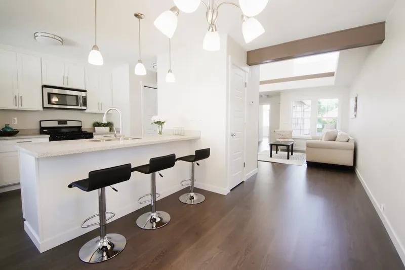 Kitchen counter with three black stools, opening past a doorway to the living room and its cream sofa