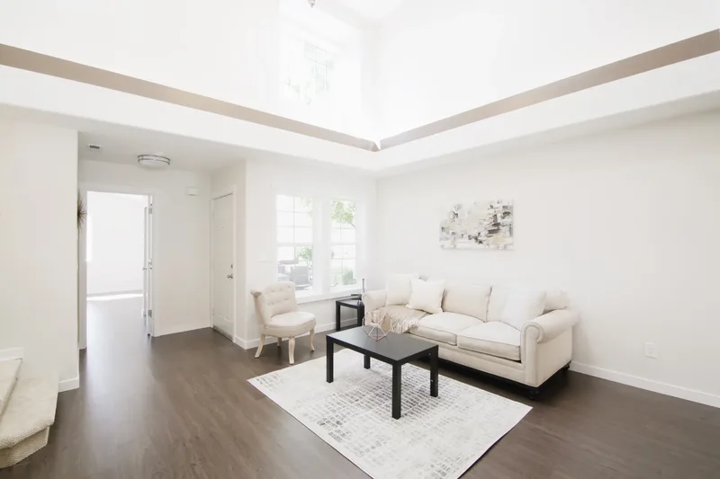 Cream sofa and black coffee table on a patterned rug, tall tray ceiling and front door at left