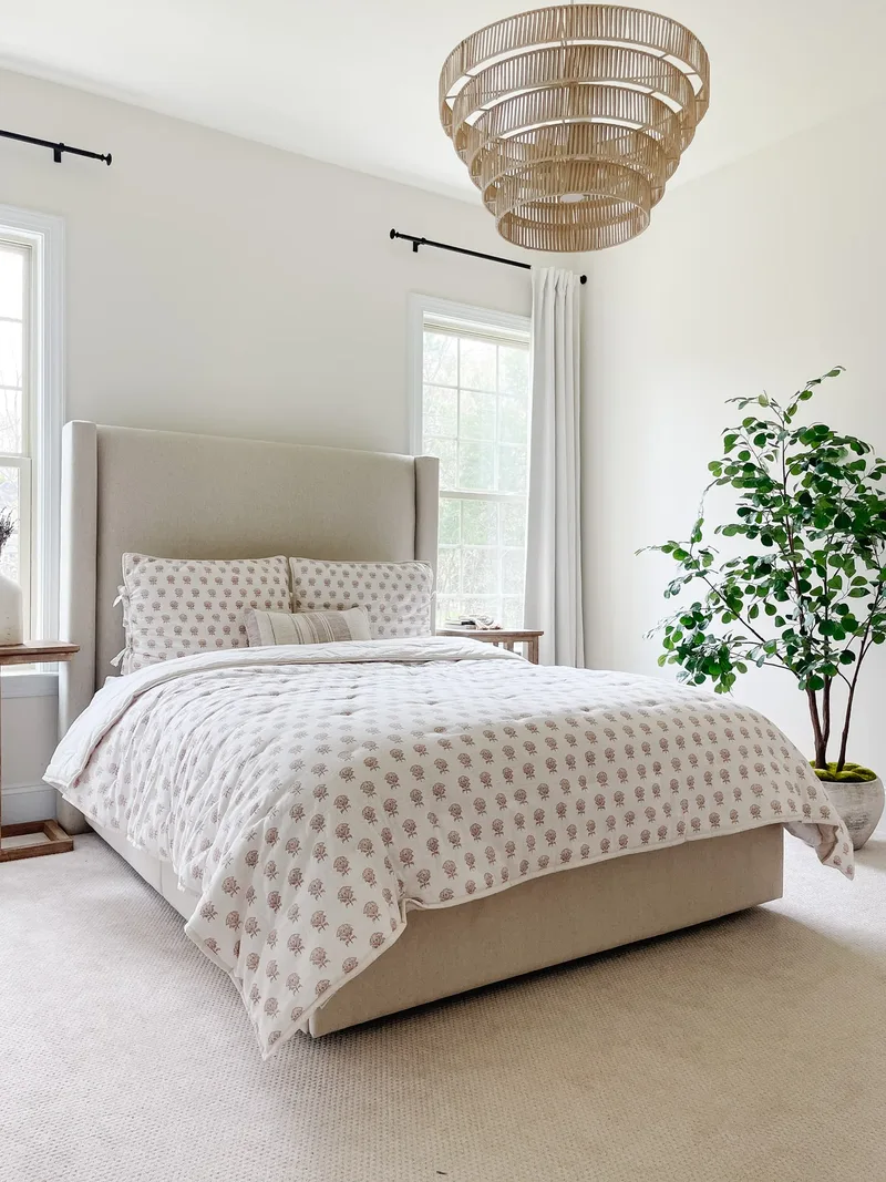 The guest room from the corner, tiered rattan chandelier overhead and the quilt turned back over cream carpet