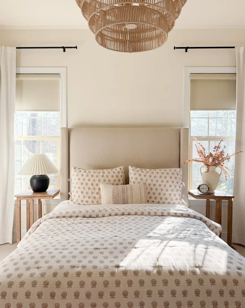Sunlight falls across the block-print quilt, the bed centred between two windows with wooden nightstands either side
