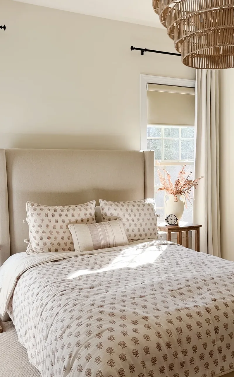 Dried branches in a cream vase and a small clock on the nightstand beside the made bed