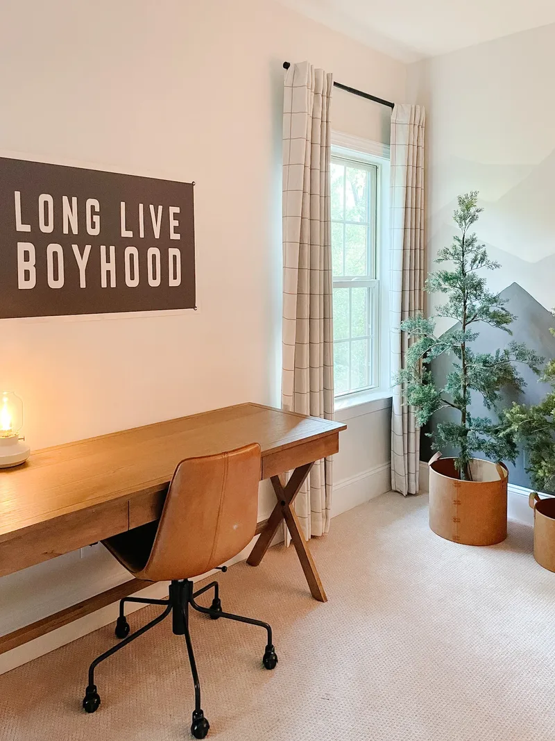 A wooden X-leg desk and tan leather task chair under a LONG LIVE BOYHOOD banner