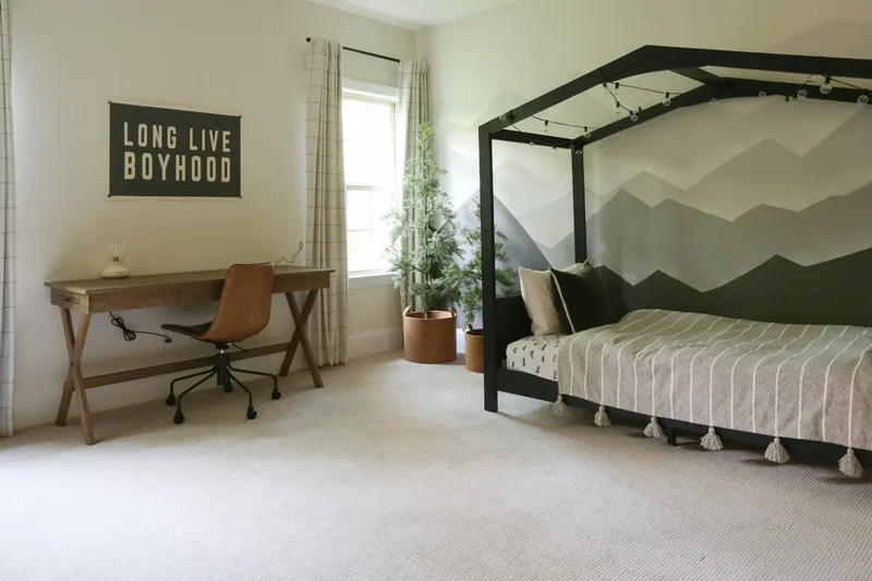 Desk wall and house-frame bed together, a striped tasselled bedspread set against the grey mountain mural