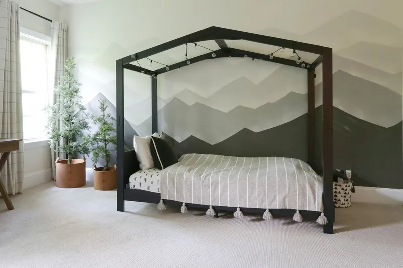 The house-frame bed close up, cafe lights along its peak and faux evergreens in leather planters