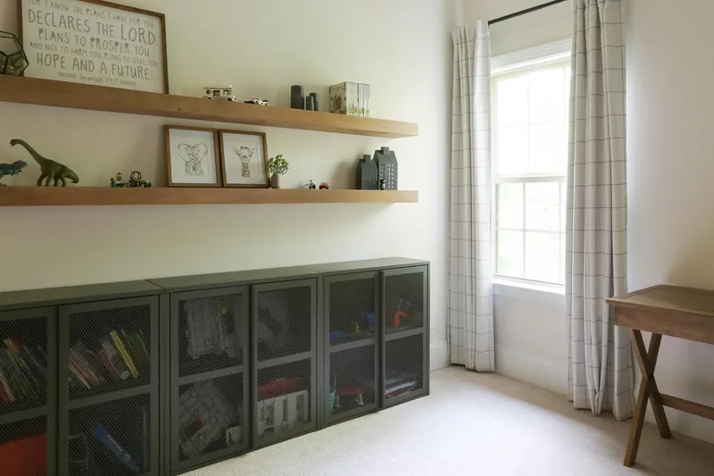 Storage wall seen from the bed side, curtained window and the corner of the desk at right
