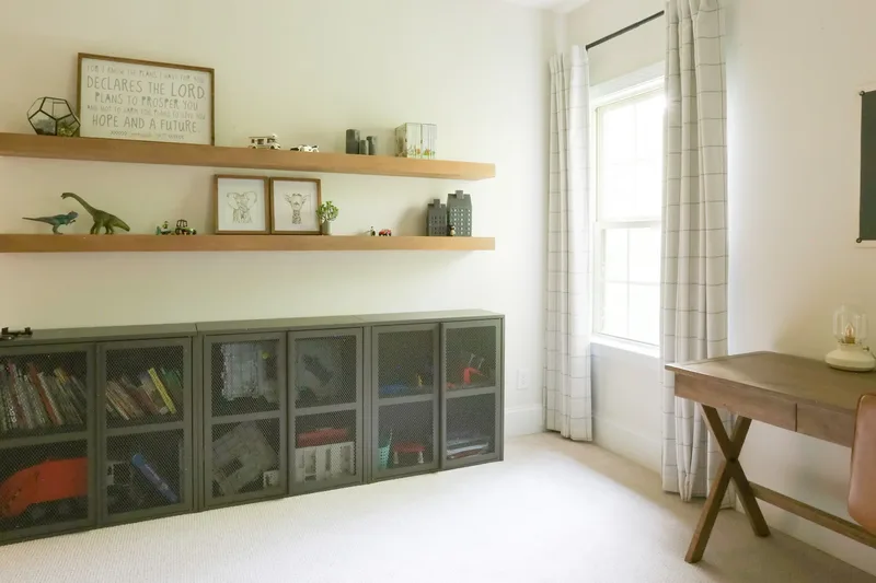 Shelves and cabinets viewed from the bed, daylight from the window falling across pale carpet