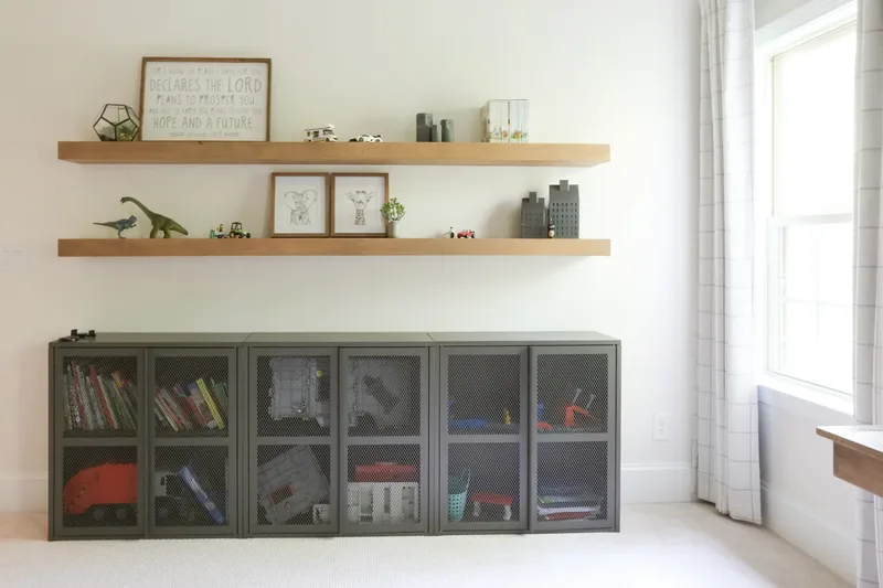 The storage wall squared up: two oak shelves above a run of mesh cabinets holding books and building bricks