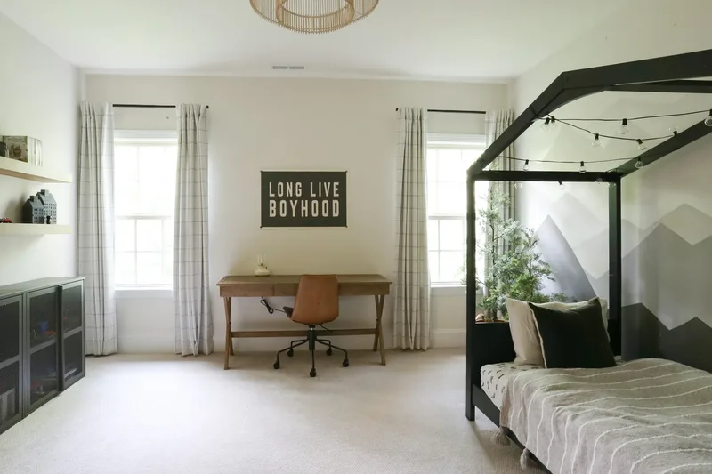 Room from the doorway, twin windows flanking the desk and the dark bed frame at right