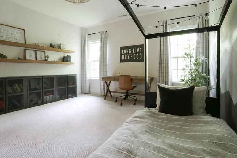 Low angle across the bed, storage wall and desk receding toward the two corner windows