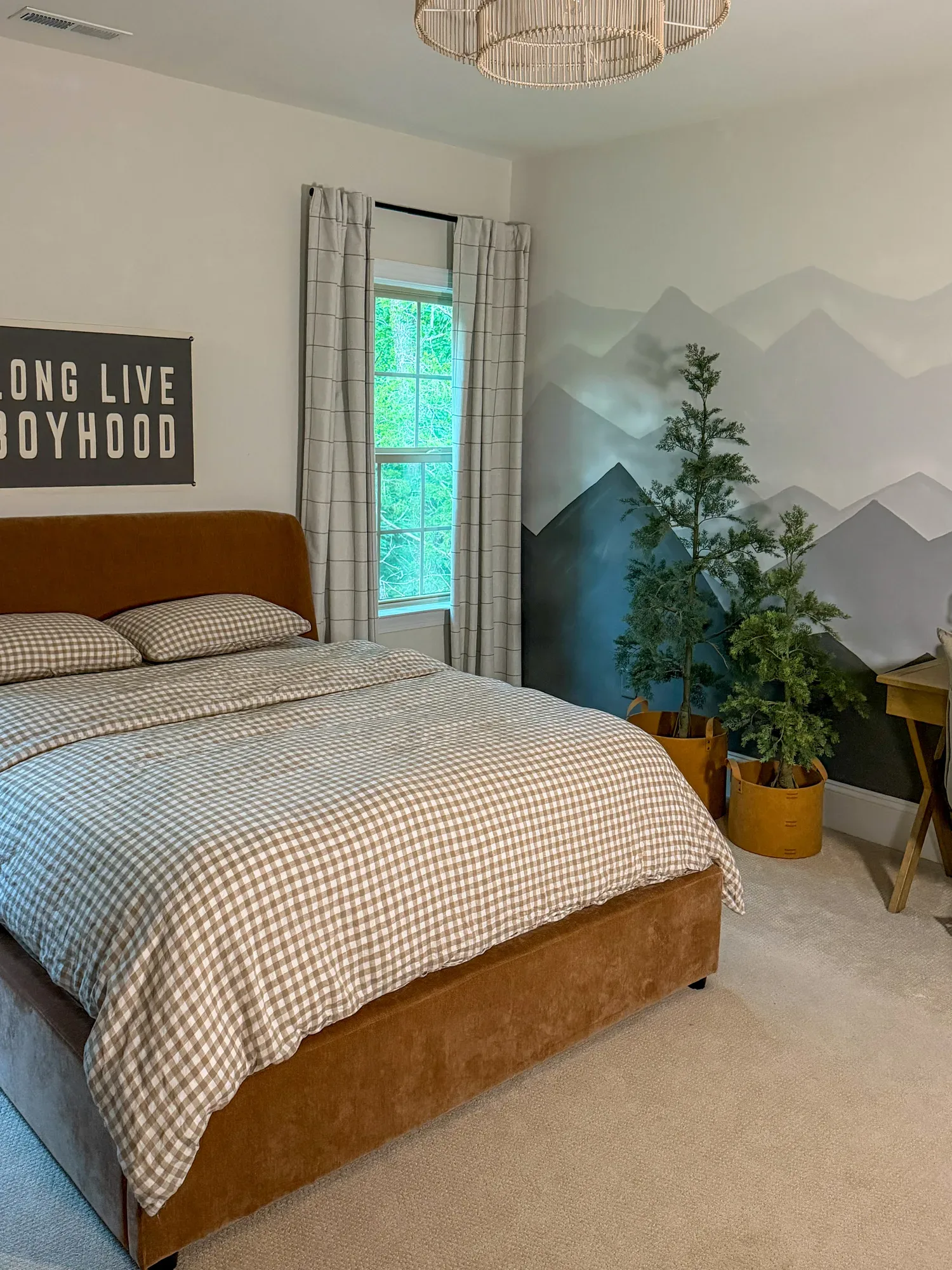 The whole bedroom: gingham-dressed bed, painted mountain mural, potted evergreens in ochre planters, woven pendant overhead