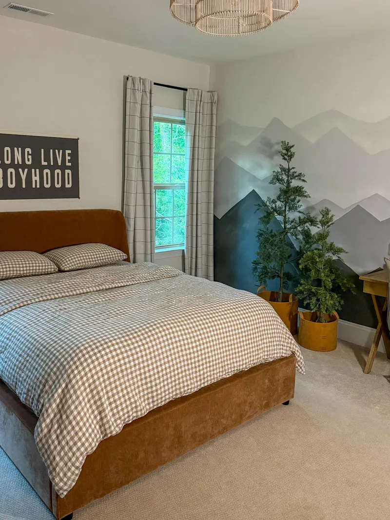 The whole bedroom: gingham-dressed bed, painted mountain mural, potted evergreens in ochre planters, woven pendant overhead