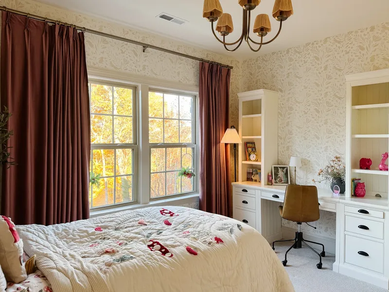 A white built-in desk between two bookcase towers, tan leather task chair, woodland wallpaper and rust velvet curtains