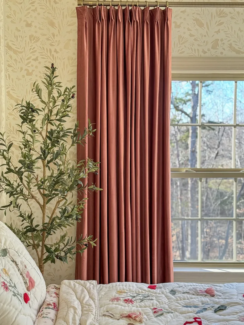 A pinch-pleated rust velvet panel beside an olive tree and rabbit-patterned wallpaper