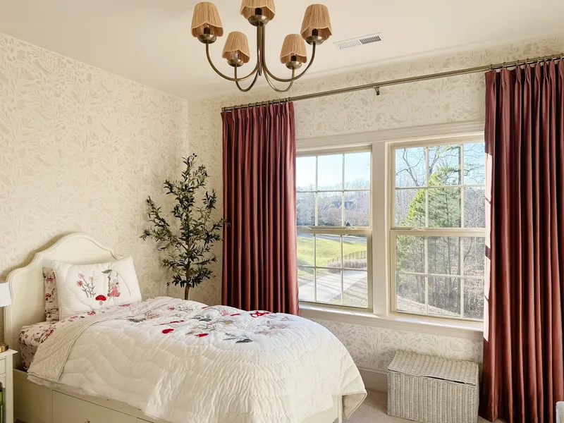 A cream bed with curved headboard and storage drawers, floral pillow, woven hamper, olive tree in the corner