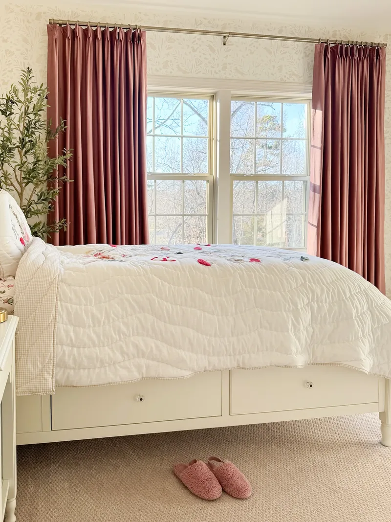The foot of the bed, two storage drawers with round knobs, pink slippers on the carpet below
