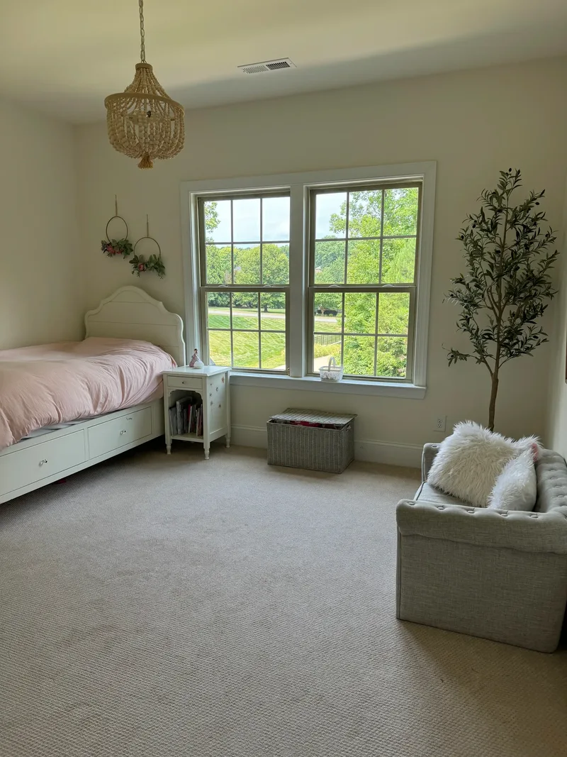 The bedroom before the makeover — plain walls, bare windows, pink duvet, beaded chandelier and a grey tufted settee