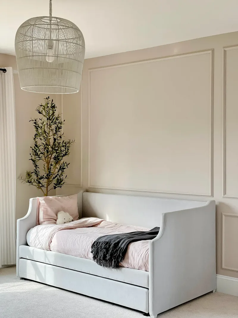 The whole daybed with its pull-out trundle, pink bedding and charcoal fringed throw, under a woven dome pendant