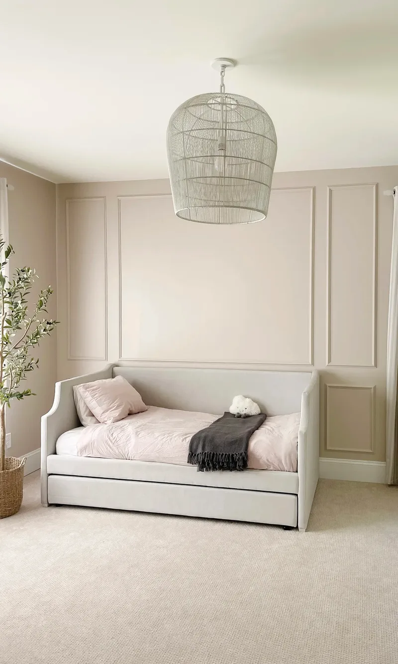 Straight-on view of the daybed centred on the panelled cream wall, oversized woven pendant hanging above it