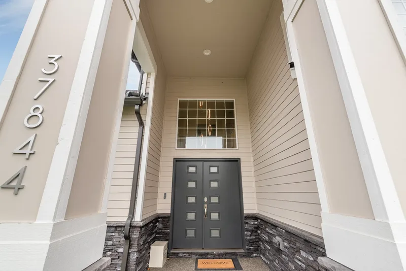 Looking up into the tall entry porch at a dark double door with square panes below a gridded transom