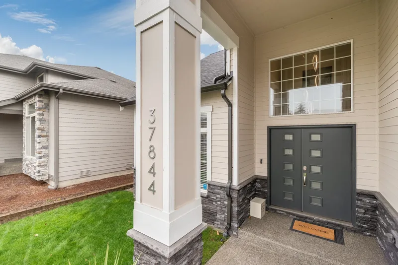 The entry seen from the walk, house numbers on the square column, stacked stone and a welcome mat