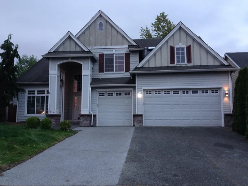 The house before the remodel, in a phone photograph: grey siding, dark red shutters and white garage doors