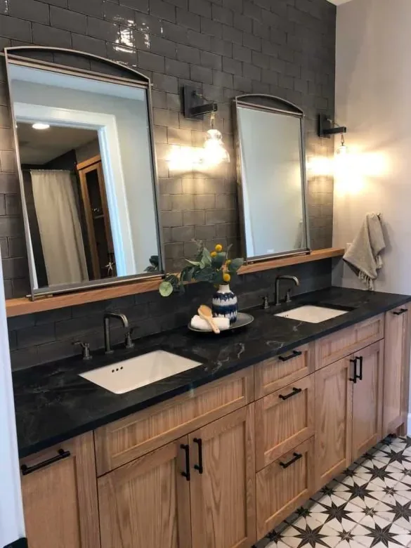 A double oak vanity against dark subway tile, arched mirrors with sconces between them