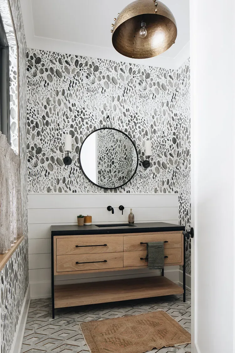 A patterned-wallpaper powder room with a round black mirror between two black sconces