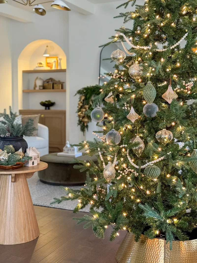 Mercury glass ornaments and beaded garland on the lit tree, a gold collar around its base