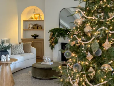 The decorated tree from across the room, past a curved sofa and olive velvet ottoman toward the mantel
