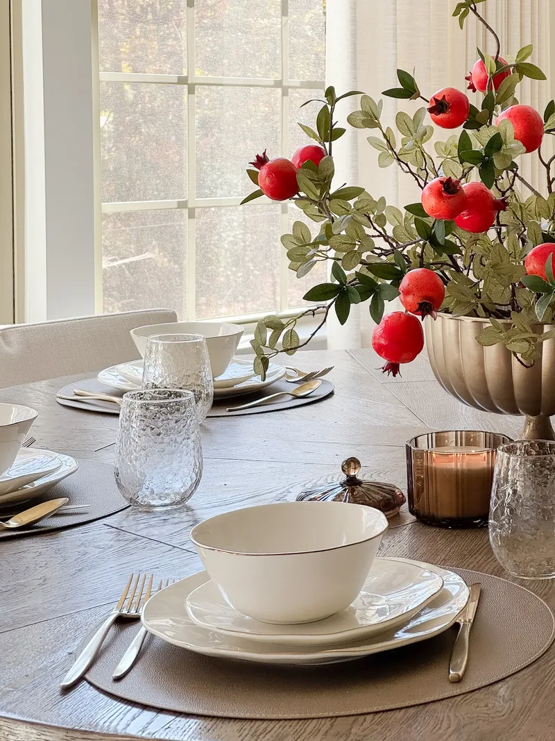 Gold-rimmed bowl on stacked plates, pomegranate centrepiece and a bright mullioned window behind