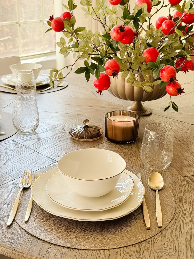 A single place setting close up, gold cutlery on a round leather mat beside a lit amber candle