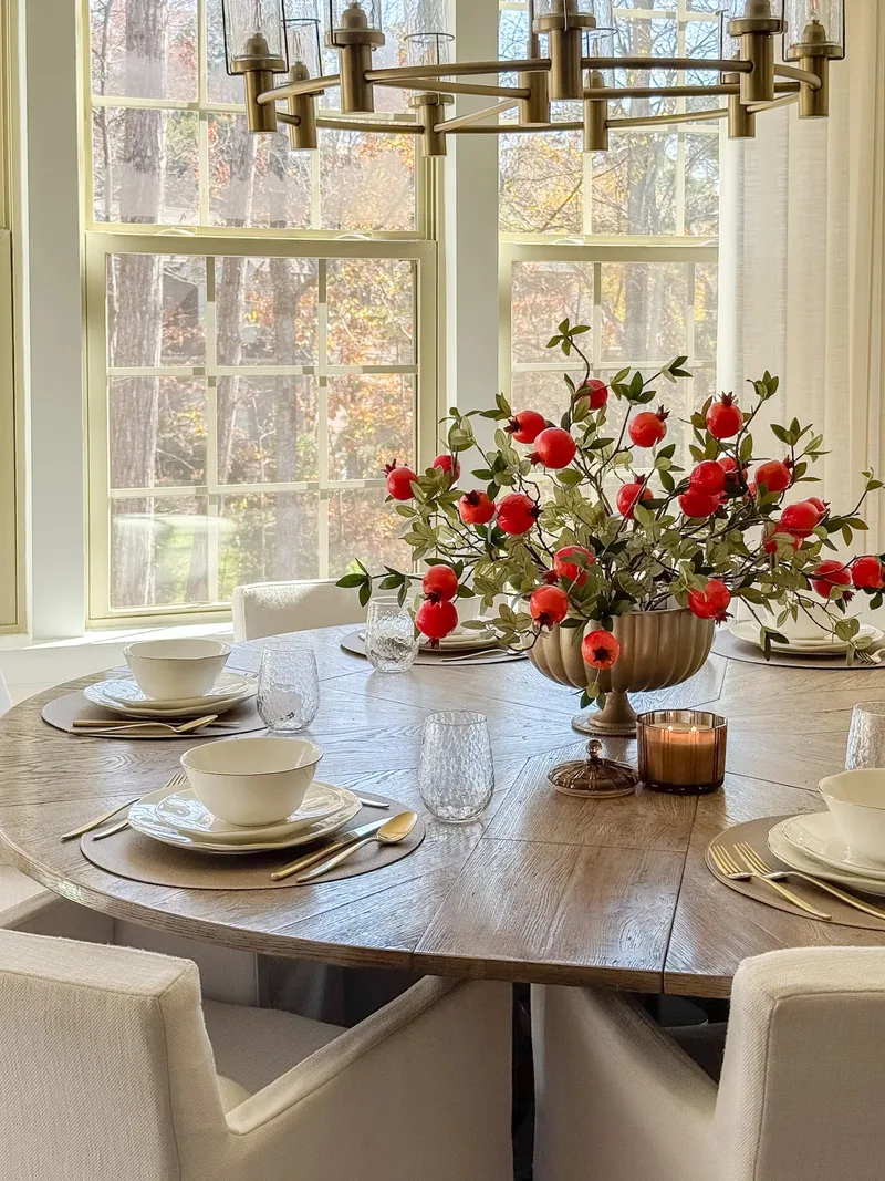 The full round table set for six, pomegranate arrangement centred beneath the brass ring chandelier