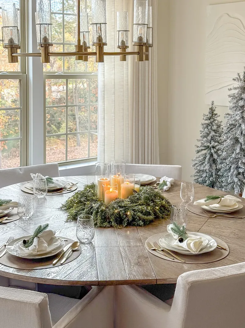 The candlelit wreath centrepiece from the opposite side, place settings and flocked trees to the right