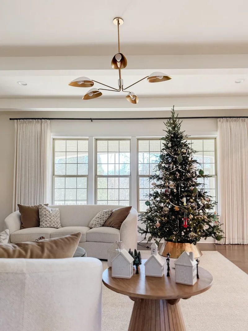Living room with a lit tree on a gold collar between windows, ceramic village houses on the coffee table