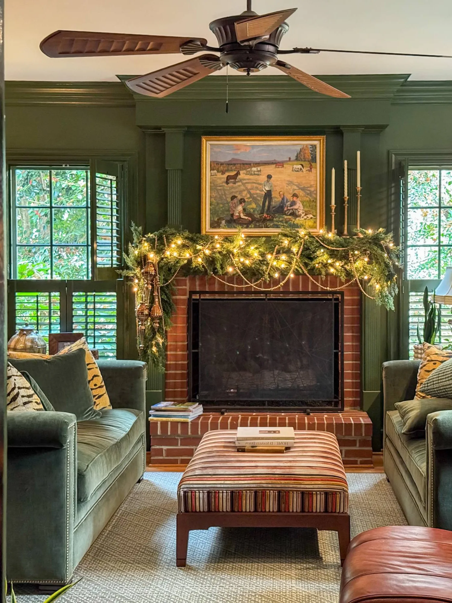 A lit cedar garland along a brick fireplace mantel in a dark green panelled living room