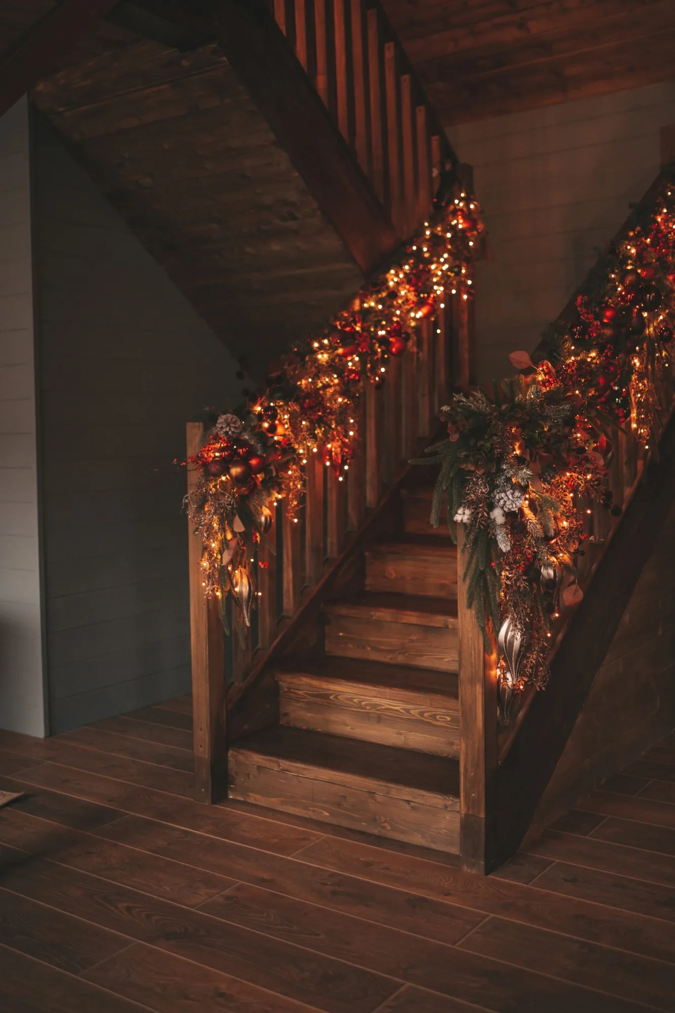 A lit garland of berries, pine cones and greenery down the rail of a dark wooden staircase