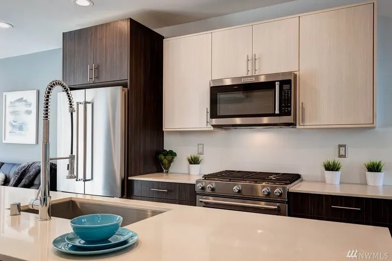Stainless gas range and microwave between pale upper cabinets and dark lower ones, seen across the island sink