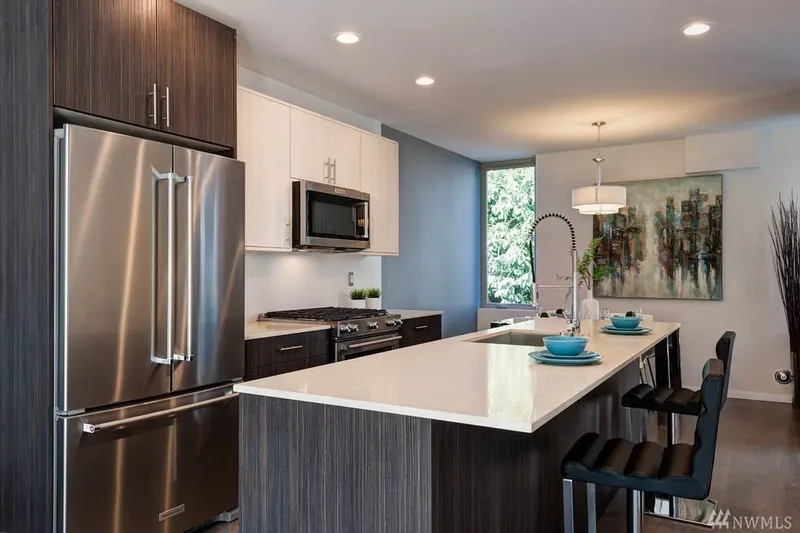 The two-tone kitchen from the refrigerator end, its long quartz peninsula lined with black stools under a drum pendant
