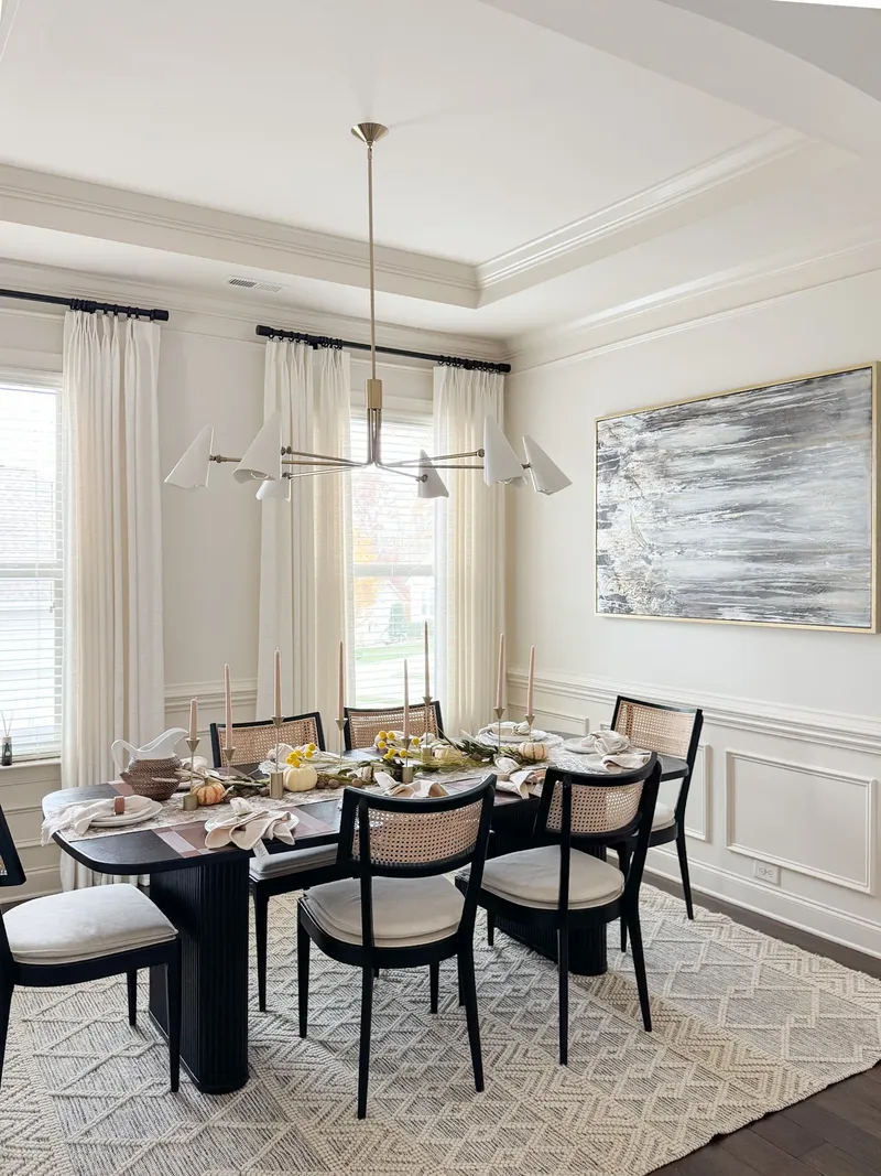 An autumn table set with taper candles and small pumpkins, black cane chairs, large abstract canvas behind