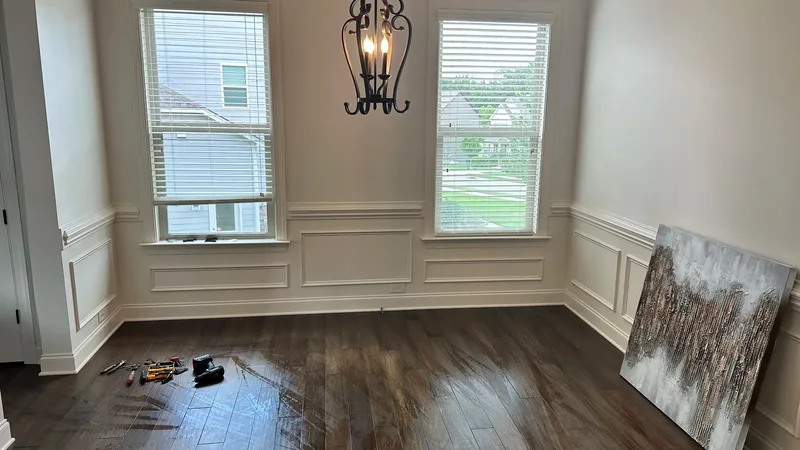 The dining room mid-project: bare wood floor with tools, old iron chandelier, the abstract canvas propped against the wainscoting