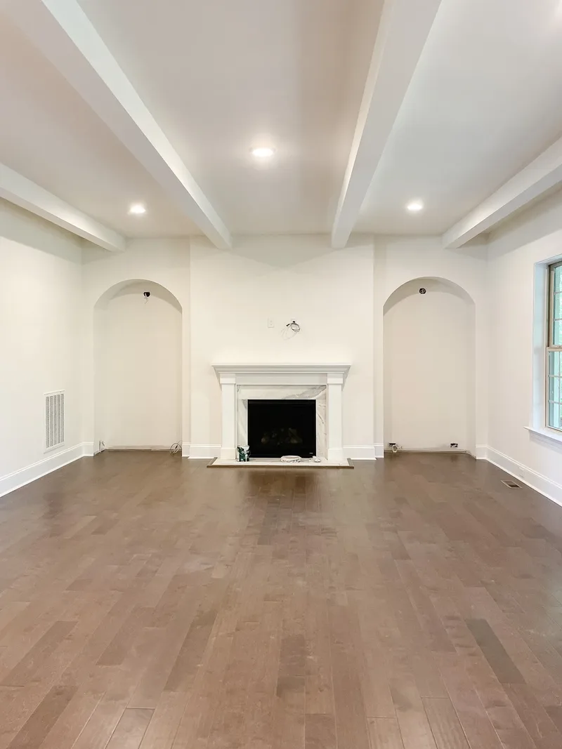 The room before furnishing — white marble fireplace flanked by two empty arched niches under painted ceiling beams