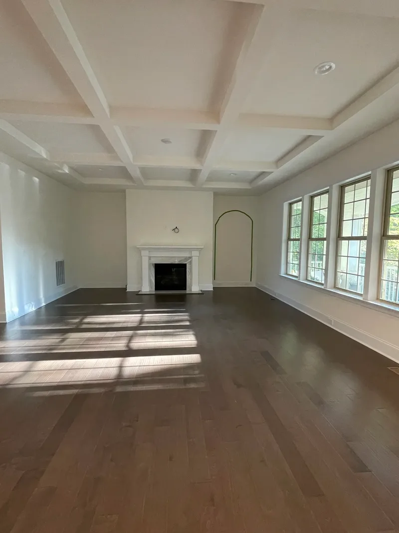 The same room mid-project, empty under a coffered ceiling, the future arch outlined in green tape beside the fireplace