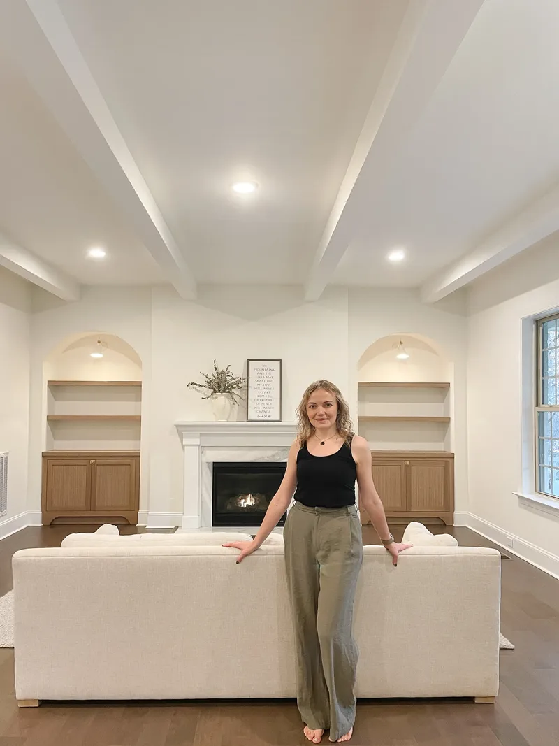 Standing behind a cream sofa, Tatyana in front of the lit fireplace and the still-bare arched built-ins