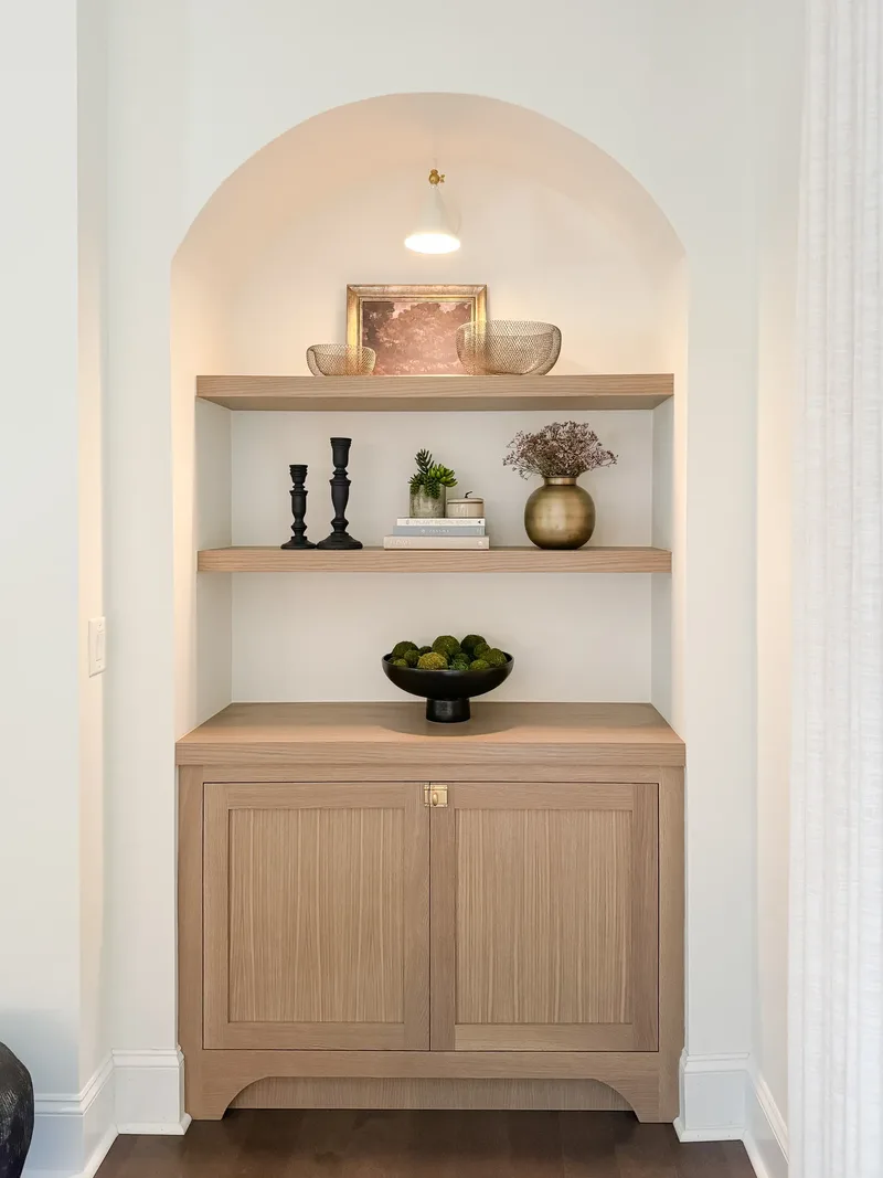 The finished alcove styled with gilt-framed art, mesh bowls, black candlesticks, a brass vase and a footed bowl