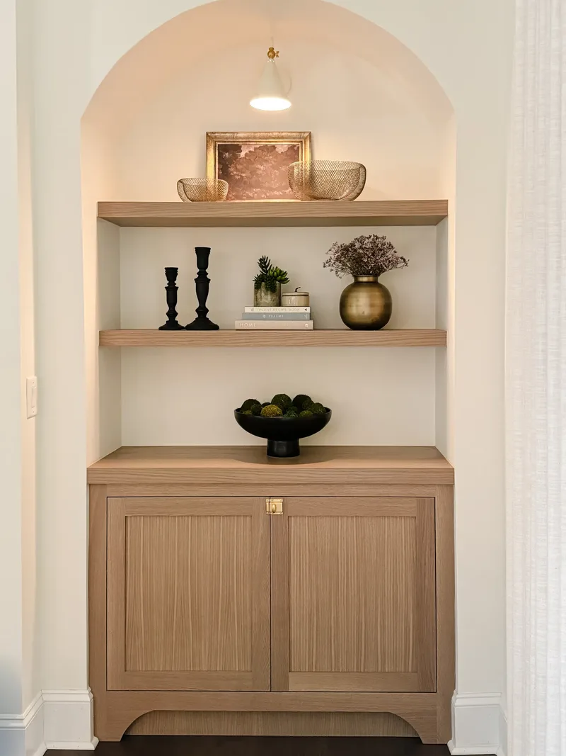 The styled alcove framed tighter, the cabinet cropped at the floor, the sconce washing light down the arch
