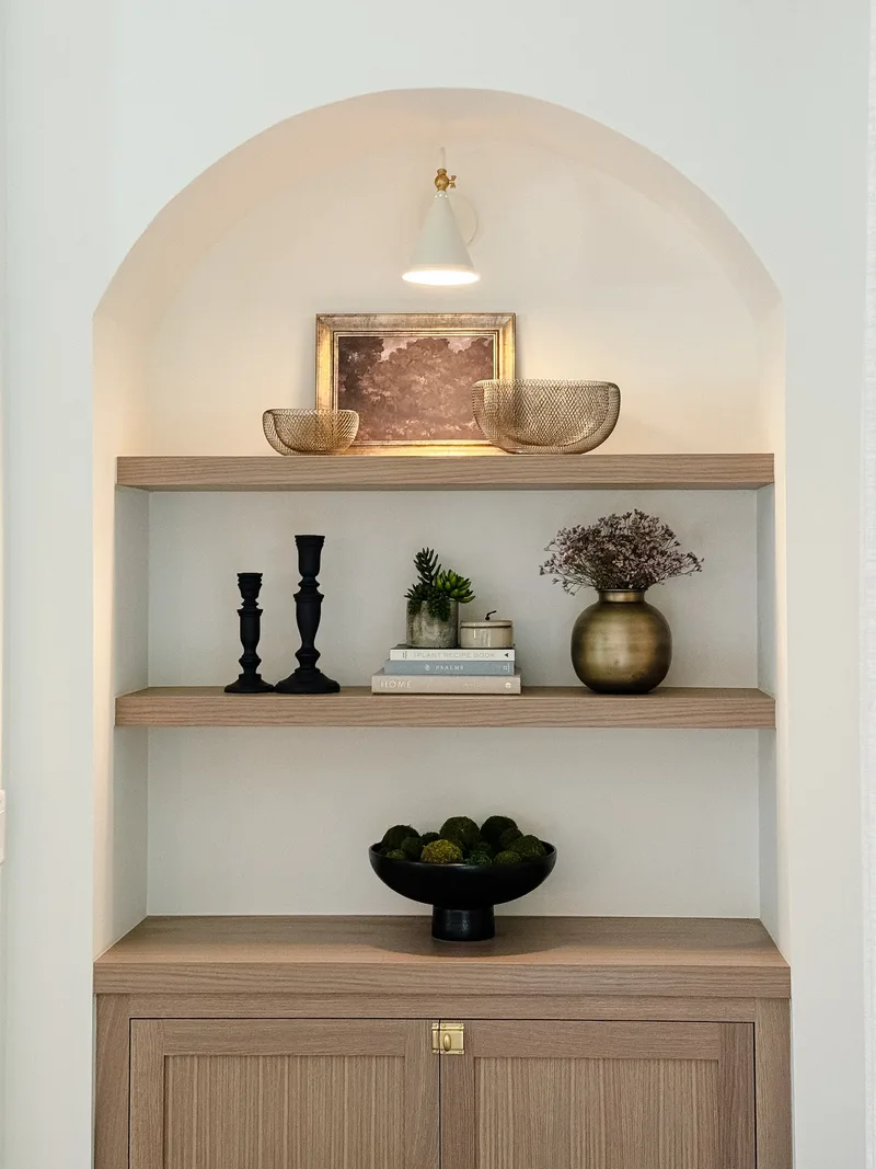 The tightest view of the shelves — black candlesticks, stacked books, a succulent and dried blooms in brass